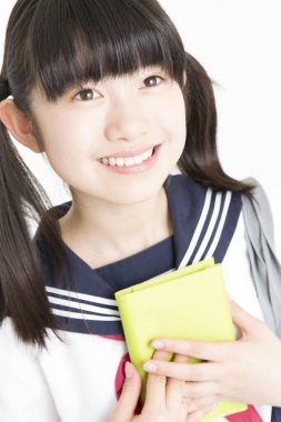 Okul üniformalı, beyaz arkaplan üzerine kitabı olan güzel bir öğrencinin portresi.