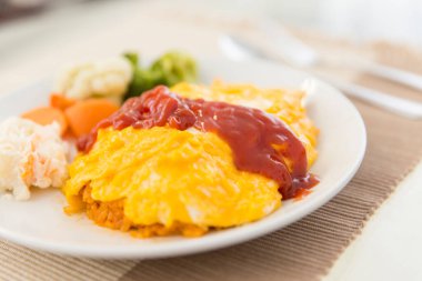 Omlet ve ketçaplı kızarmış et aşısı, beyaz tabakta buharda pişmiş sebze. 