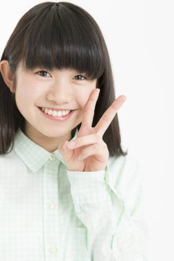 Genç Asyalı kız öğrenci beyaz arka planda izole edilmiş zafer işareti gösteriyor. 