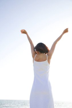 Sahilde kollarını kaldırmış, arkadan bakan bir kadın.