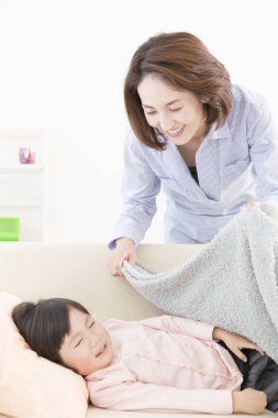 Asyalı anne kızını battaniyeyle örtüyor. 