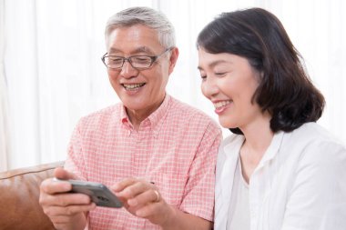 Mutlu Asyalı kadın ve erkek evde akıllı telefon kullanıyor. 