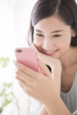 Asyalı kadın evde akıllı telefona bakıyor. 