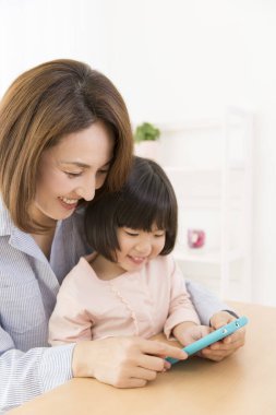 Asyalı anne ve kızı telefon kullanıyor.