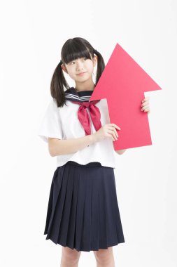 Okul üniformalı küçük Asyalı kız elinde kırmızı ok işareti var, beyaz arka planda izole edilmiş.