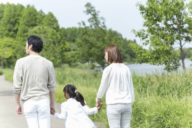 Mutlu Asyalı anne, baba ve kız parkta birlikte vakit geçiriyorlar.