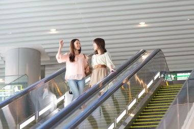 Mutlu Asyalı kadın ve yürüyen merdivendeki genç arkadaş