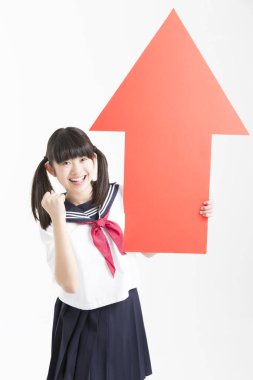 Okul üniformalı küçük Asyalı kız elinde kırmızı ok işareti var, beyaz arka planda izole edilmiş.