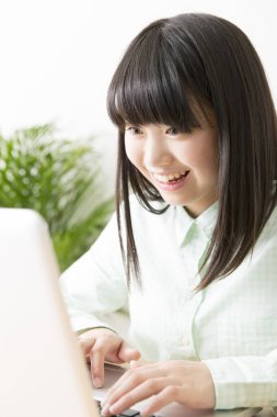 Gülümseyen Japon kız dizüstü bilgisayarla masada oturuyor.