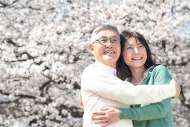 Güzel Asyalı olgun çift çiçek açan kiraz ağaçlarına karşı poz veriyor.