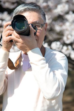 Olgun Asyalı fotoğrafçı parkta fotoğraf çekiyor.