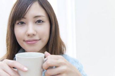 Elinde kahve fincanı olan genç Asyalı kadın.