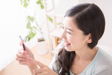 Genç Asyalı kadın odada akıllı telefon kullanıyor. 