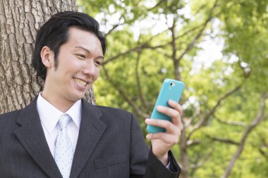 Parkta akıllı telefonu olan bir iş adamı.