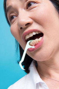 asian woman  using dental Floss pick,  blue isolated background 