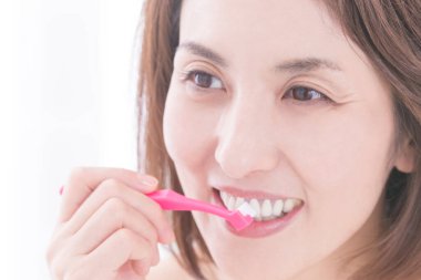 Güzel Japon kadın beyaz arka planda dişlerini fırçalıyor.