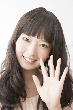 Asyalı genç kadın gülümseyip el sallıyor.