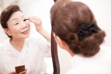 Asyalı son sınıf öğrencisi yüzüne makyaj yapıyor.