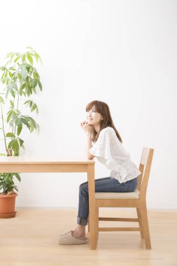 Genç Asyalı kadın evde masada oturuyor. 