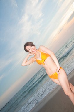 Plajda turuncu mayo giymiş Asyalı genç bir kadın. 