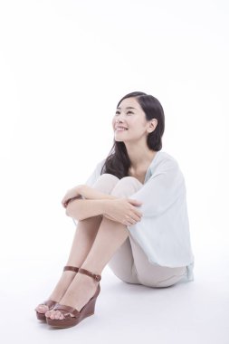 Genç Asyalı bir kadının portresi stüdyoda yerde, beyaz arka planda izole bir şekilde oturuyor.