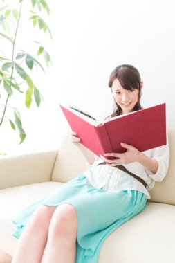 Asyalı kadın evde kitap okuyor.