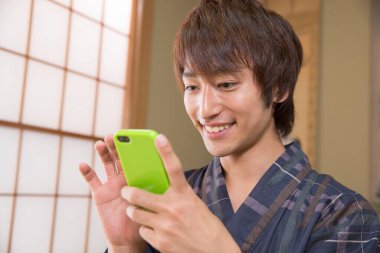 Geleneksel Yukata 'daki yakışıklı Japon genç adamın portresi. Etnik kaplıca otelinde akıllı telefon kullanıyor.