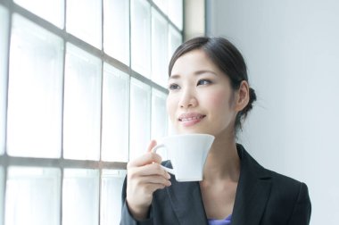 Arka planda kahve fincanı olan genç bir kadın. 