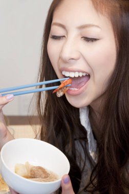 Yemek çubuğu ve çorbayla karides yiyen kadın.