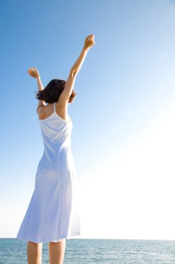 Kolları havada, kumsalda eğlenen mutlu kadın.