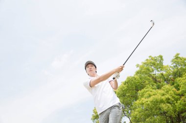 Asyalı erkek golfçü yeşil golf sahasında golf oynuyor