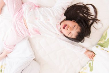 Küçük Asyalı çocuk yatağa uzanıyor. 