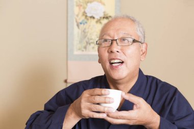 Asyalı adam elinde bir fincan çay tutuyor..