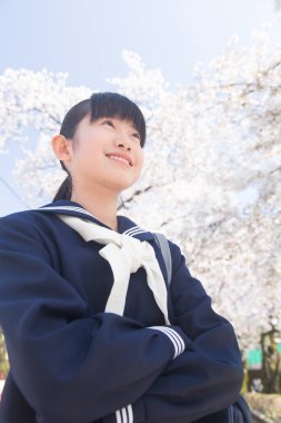 Sokakta çiçek açan kiraz ağaçlarıyla güzel Japon öğrencinin portresi.