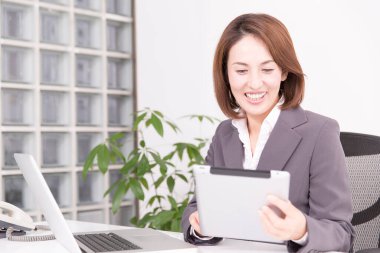 Ofiste tablet kullanan takım elbiseli Japon iş kadını.