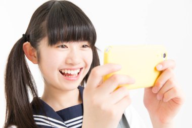 Okul üniformalı, cep telefonu kullanan Asyalı bir kızın portresi.