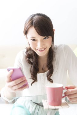 Genç kadın akıllı telefon kullanıyor ve kahve içiyor.