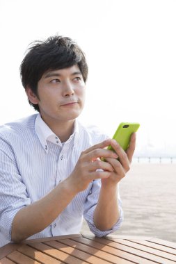 Deniz kıyısında cep telefonu kullanan Asyalı adam.