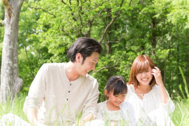 Mutlu Asyalı anne, baba ve kız parkta birlikte vakit geçiriyorlar.