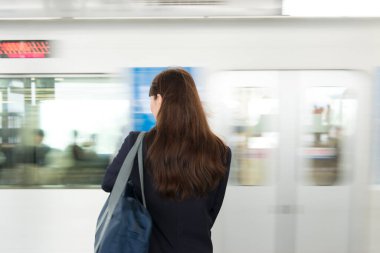 Asyalı kadın öğrenci metro istasyonunda tren bekliyor.