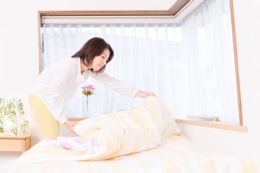 asian woman making bed at home 