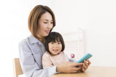 Asyalı anne ve kızı telefon kullanıyor.