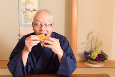 Geleneksel Japon yemekleriyle evdeki ahşap masada oturan kıdemli bir adamın portresi.