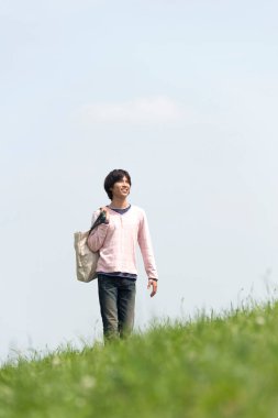Genç Asyalı adam çayırda yürüyor.