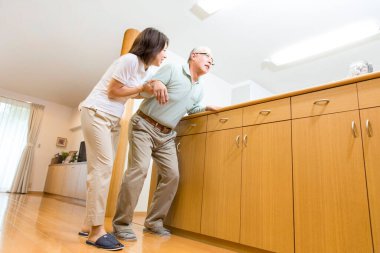 Asyalı kadın bakıcı yaşlı adamın yürümesine yardım ediyor.