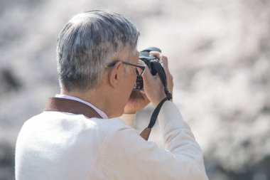 Olgun Asyalı fotoğrafçı parkta fotoğraf çekiyor.