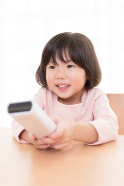 Küçük Asyalı kız uzaktan kumanda kullanıyor.