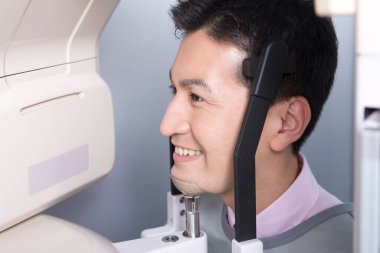 Asyalı adam gülümseyen bir makineye bakıyor, çenesinin 3 boyutlu resmini yapıyor.