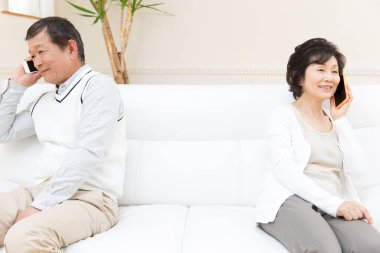 Evde cep telefonuyla konuşan yaşlı çift. 