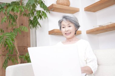 Evde dizüstü bilgisayar kullanan yaşlı bir kadın.